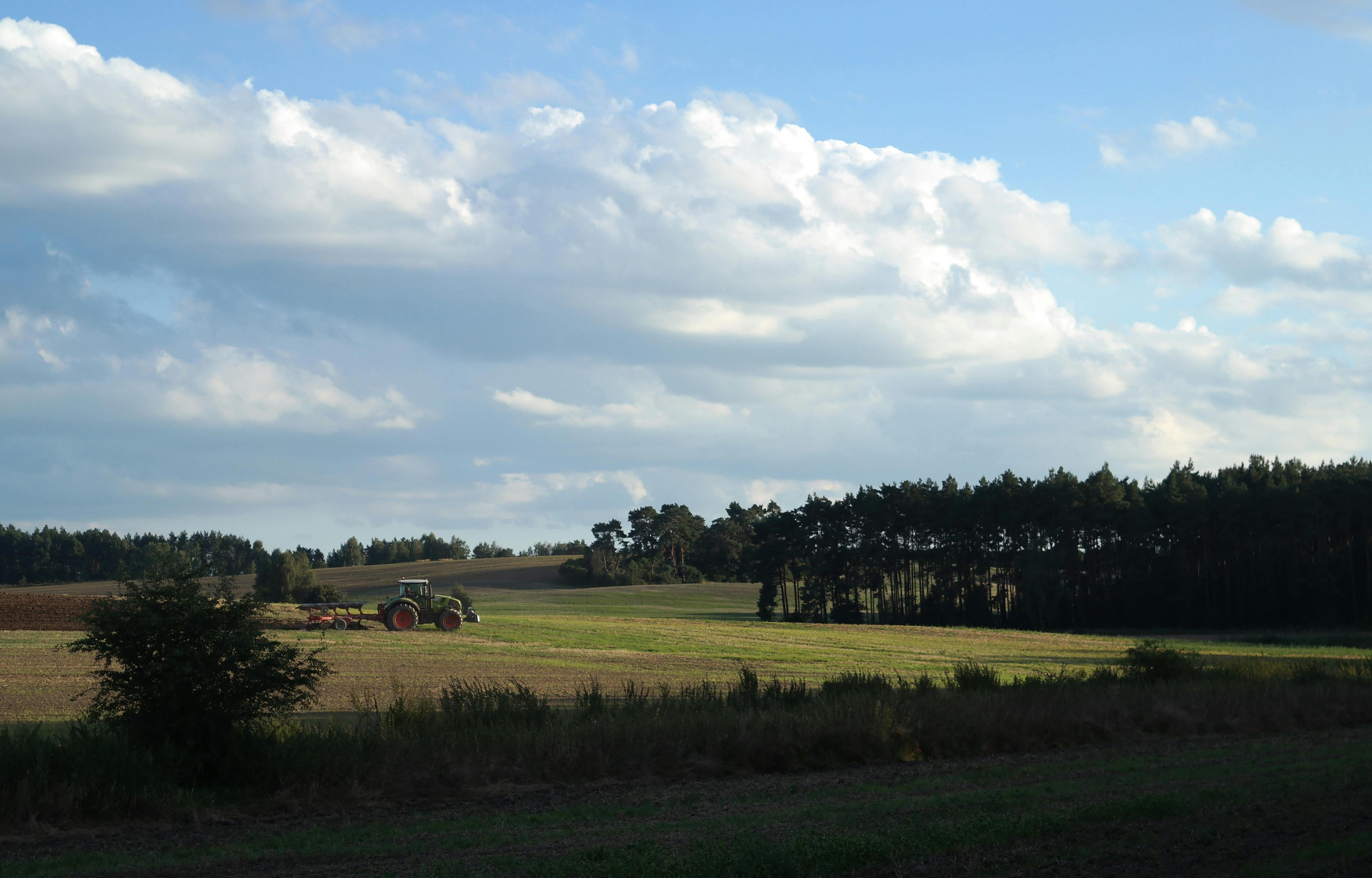 Tractor plowing a tranquil field under a bright sky, surrounded by nature.