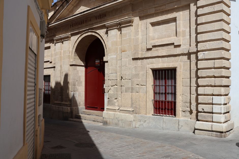 La Pescadería Vieja de Jerez de la Frontera muestra una arquitectura clásica con una atrevida puerta roja y una fachada de piedra.