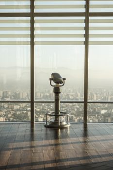透过现代建筑的大窗户，一台投币式双筒望远镜俯瞰着城市天际线