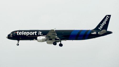 Free Black airplane with 'teleport it.' branding in flight against a cloudy sky. Stock Photo