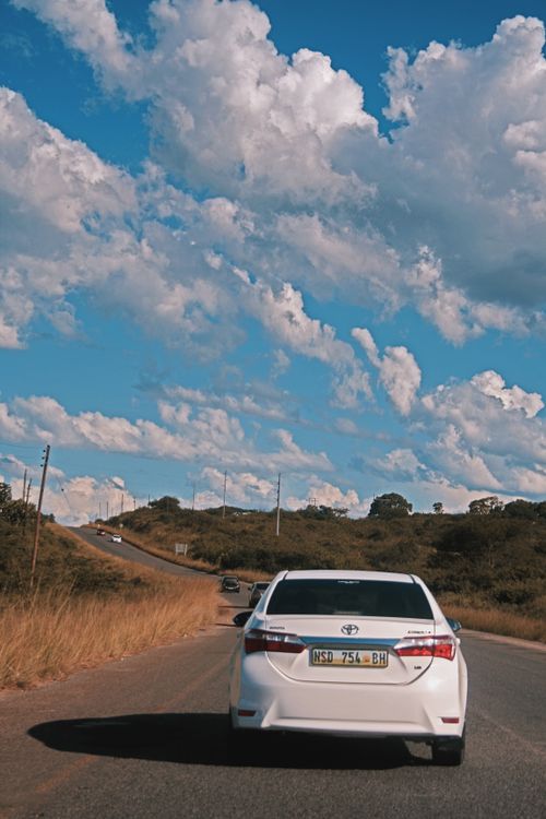 Free A car driving on a rural road in Mbabane, under a bright blue sky with clouds. Stock Photo