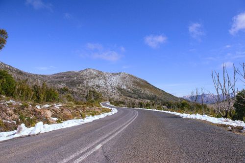 Free Winding road through snow-dusted mountains in Tasmania's wilderness under a clear blue sky. Stock Photo