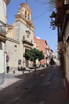 Charming narrow street in Jerez de la Frontera, featuring a historic church under a clear blue sky.