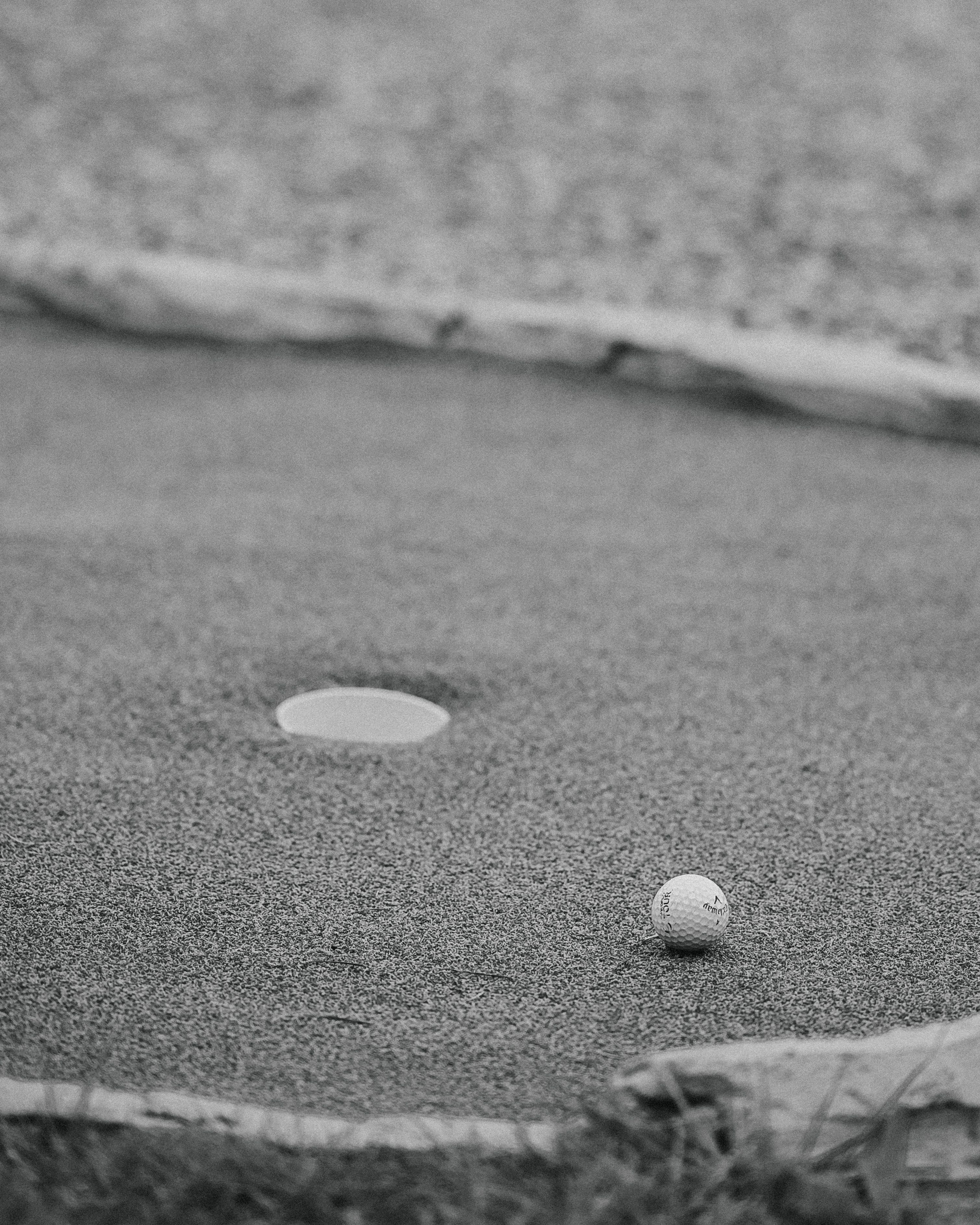 A black and white photo of a golf ball near the hole on a putting green, evoking a classic sports feel.