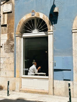 Sunlit café window in Lisbon with a person enjoying a drink inside.