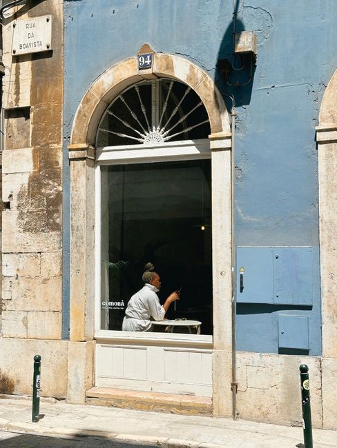 Sunlit café window in Lisbon with a person enjoying a drink inside.