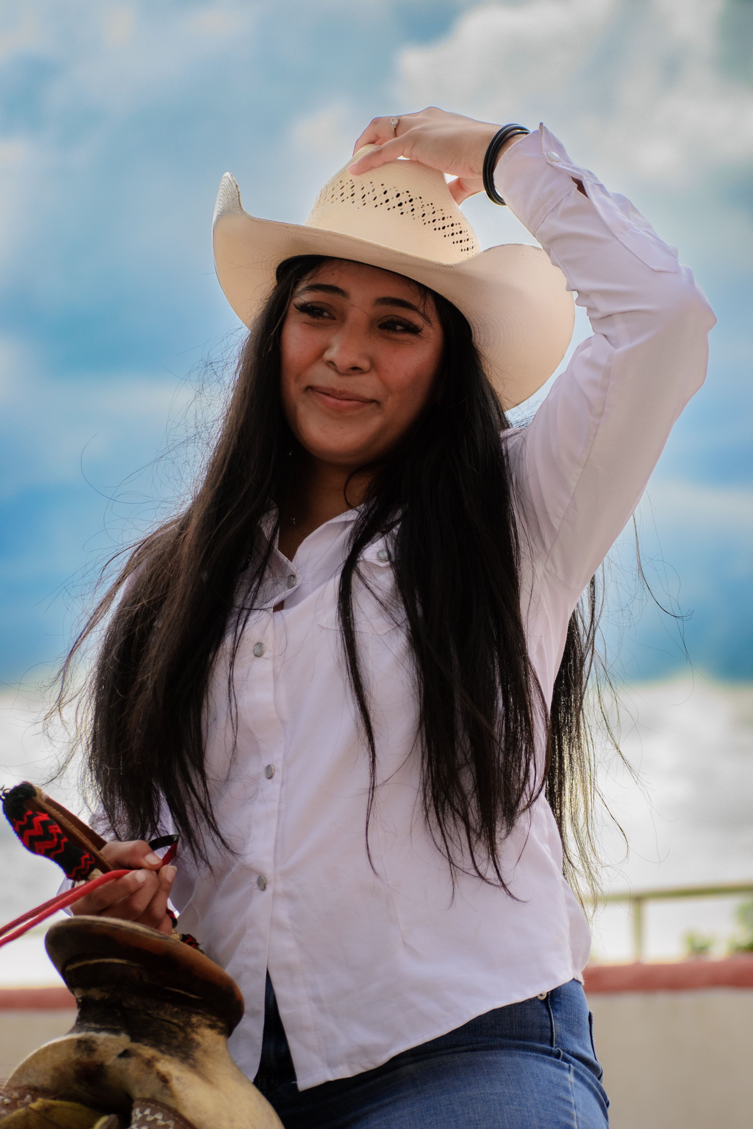A young woman with long hair and a cowboy hat enjoying a sunny day outdoors, capturing a blend of modern fashion and tradition.