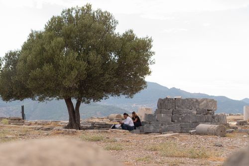 Free Visitors rest under a tree amidst ancient stone ruins in Izmir, Türkiye. Stock Photo