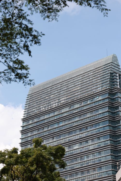 Free A sleek modern office building with glass facade on a clear day with blue sky and greenery. Stock Photo
