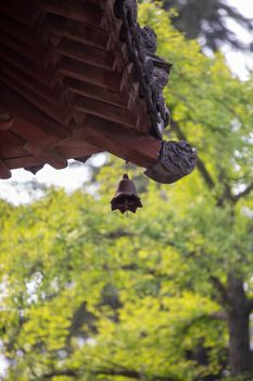A traditional temple roof with a decorative bell, set against lush green foliage, showcasing classic architecture.