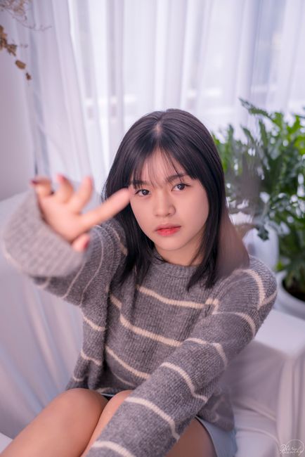 Young woman in a striped sweater reaching towards the camera in a cozy indoor setting.