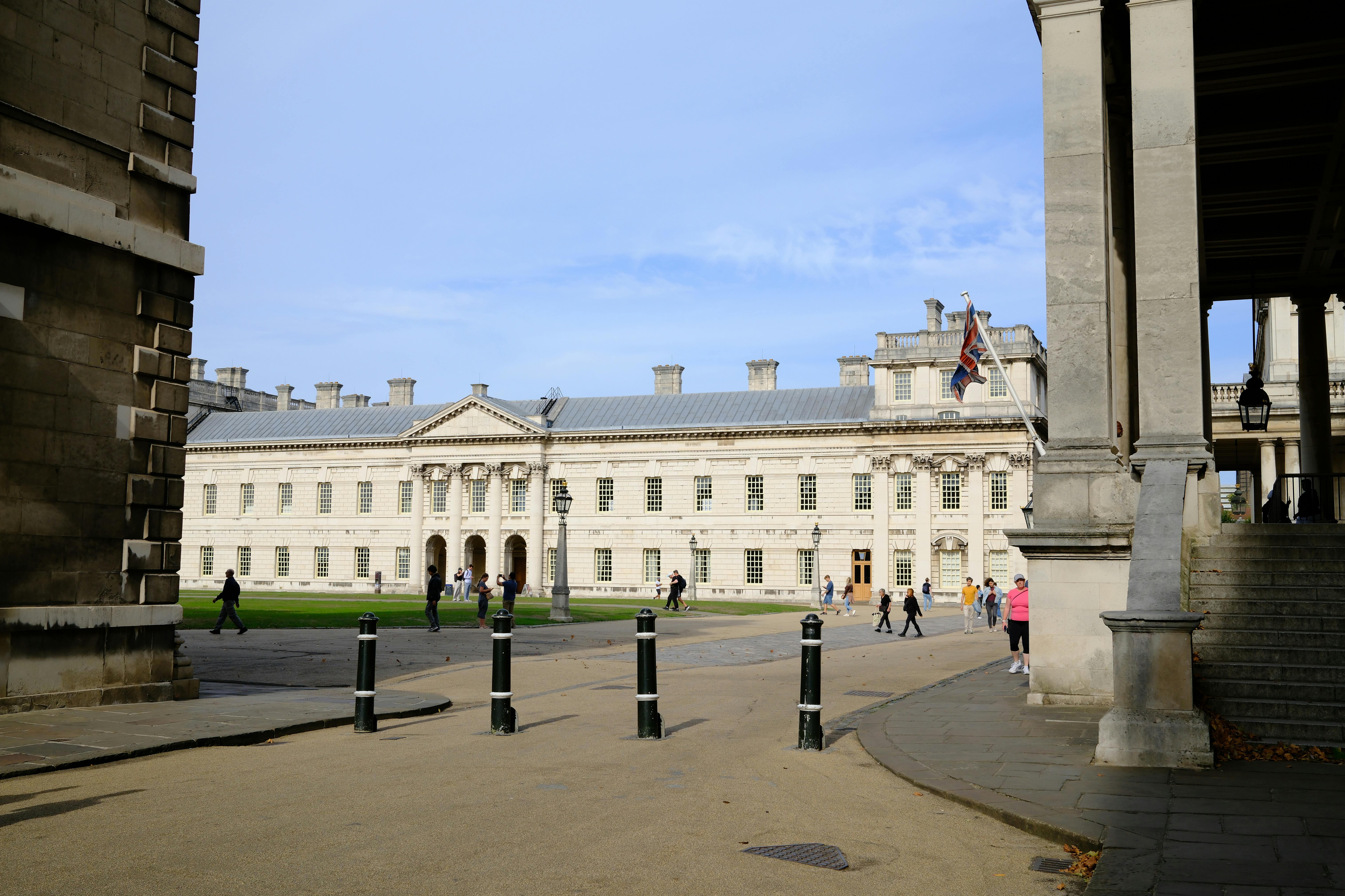 People walking near a historic building displaying the Union Jack under a clear blue sky.