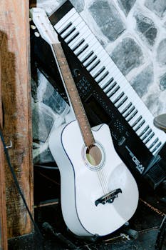 A white acoustic guitar leaning against a keyboard on a stone background, exuding a musical ambiance.