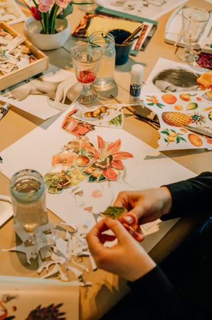 Hands creating an artistic collage with various cutouts on a table filled with art supplies.