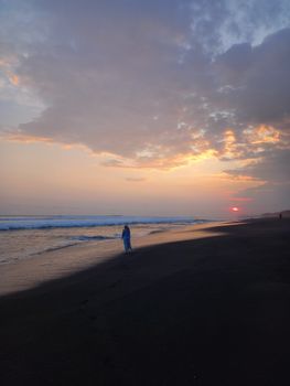 A serene beach scene at sunset with a person walking along the shore, creating a peaceful mood.