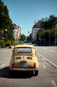 Rear view of a classic yellow car parked on a serene European street with historic architecture.