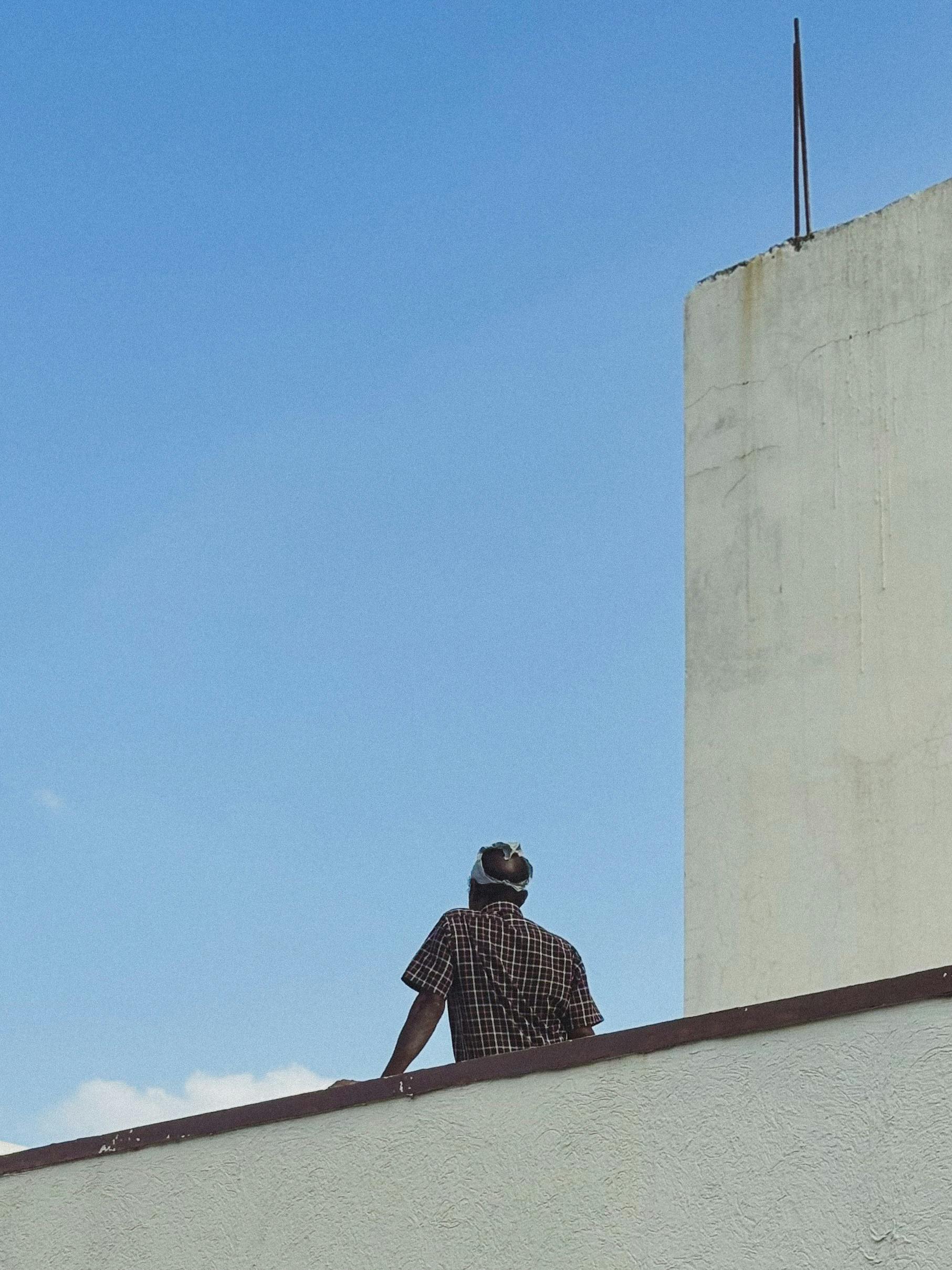 Gratis Un operaio edile è in piedi su un tetto sotto un cielo azzurro e limpido a Hyderabad, in India. Foto a disposizione