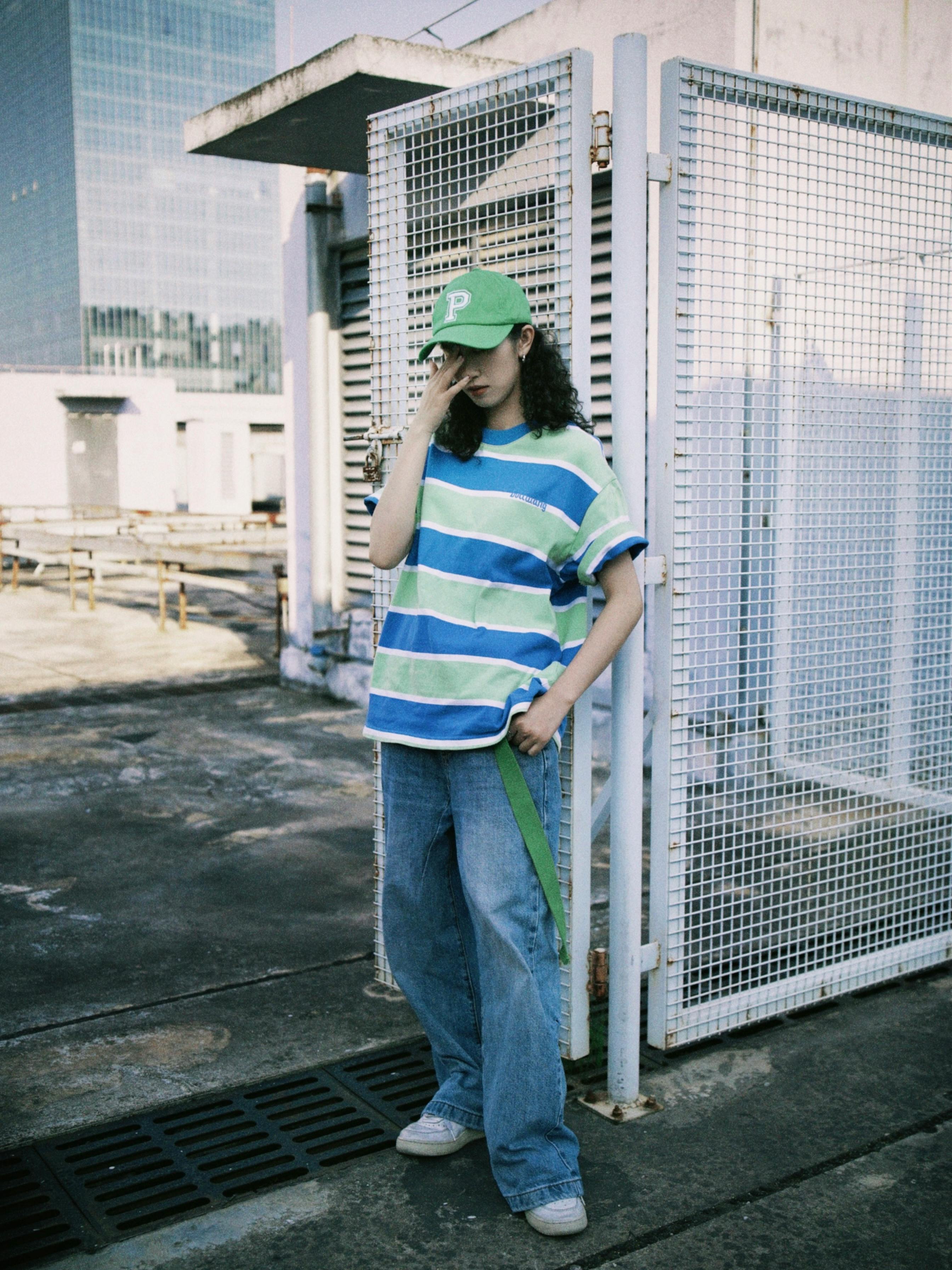 Young woman in striped shirt and cap posing on urban rooftop.