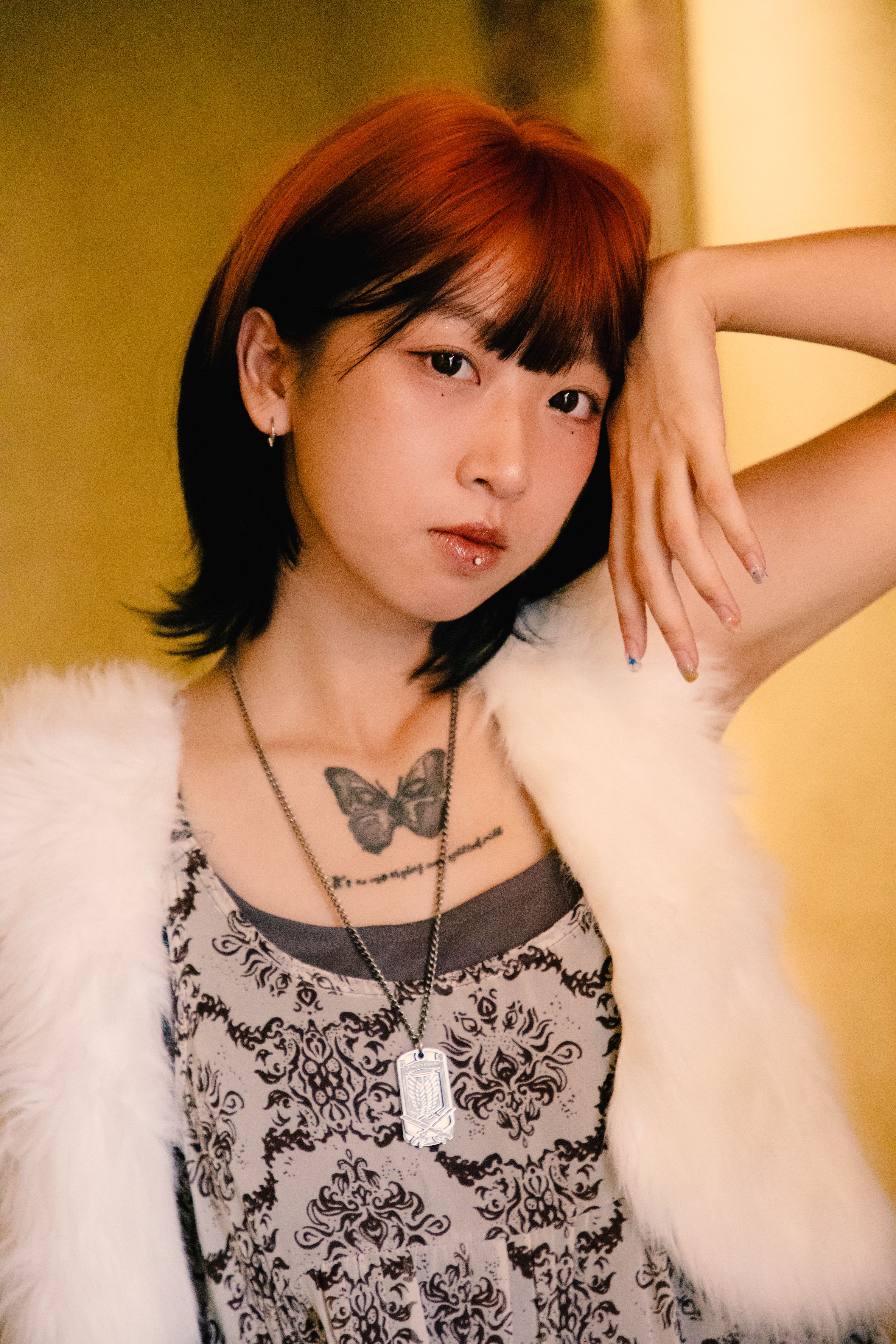 Stylish young woman poses confidently indoors, showcasing a butterfly tattoo and trendy fashion.
