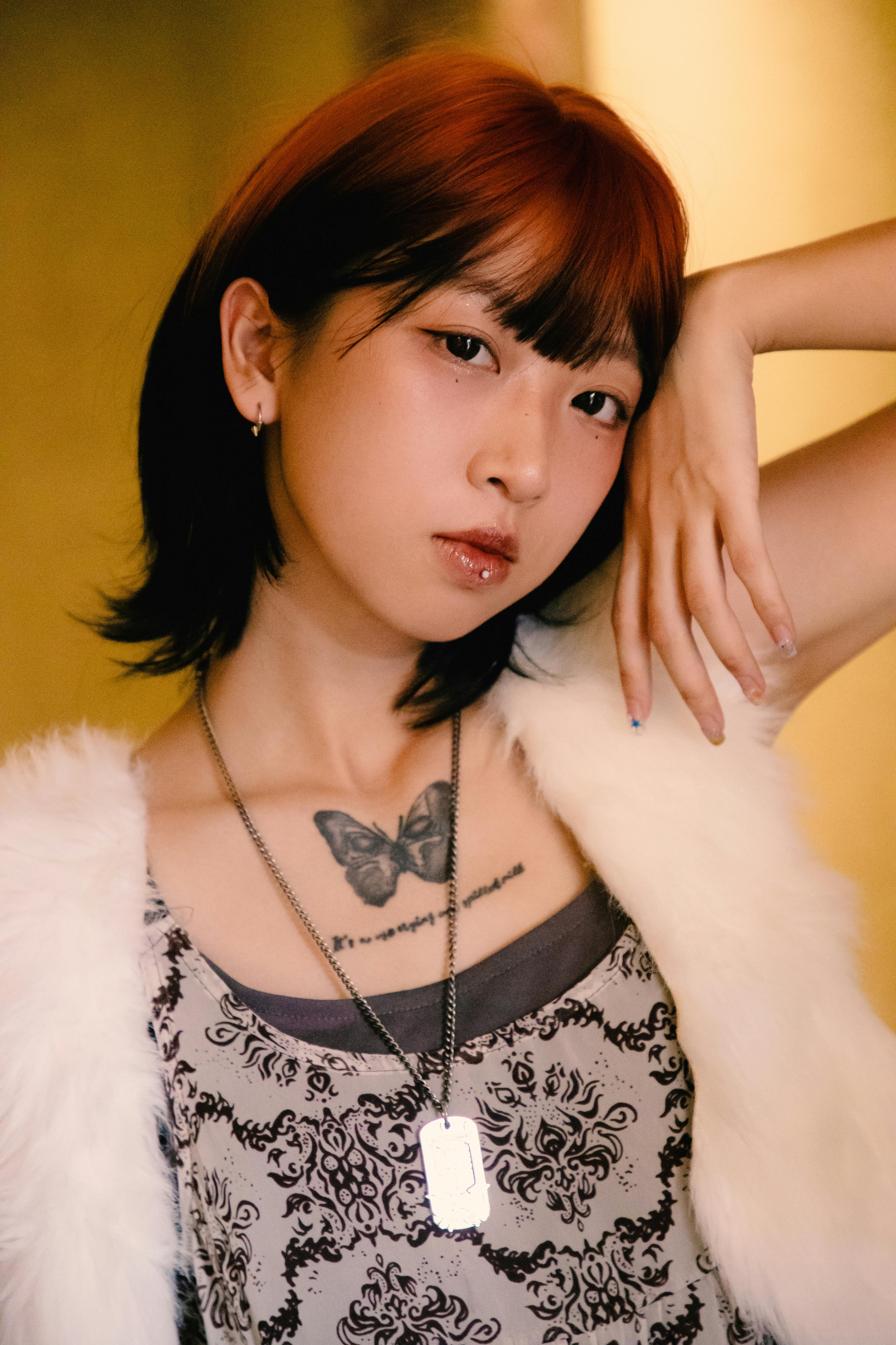 Portrait of a young woman with a butterfly tattoo and unique haircut indoors.