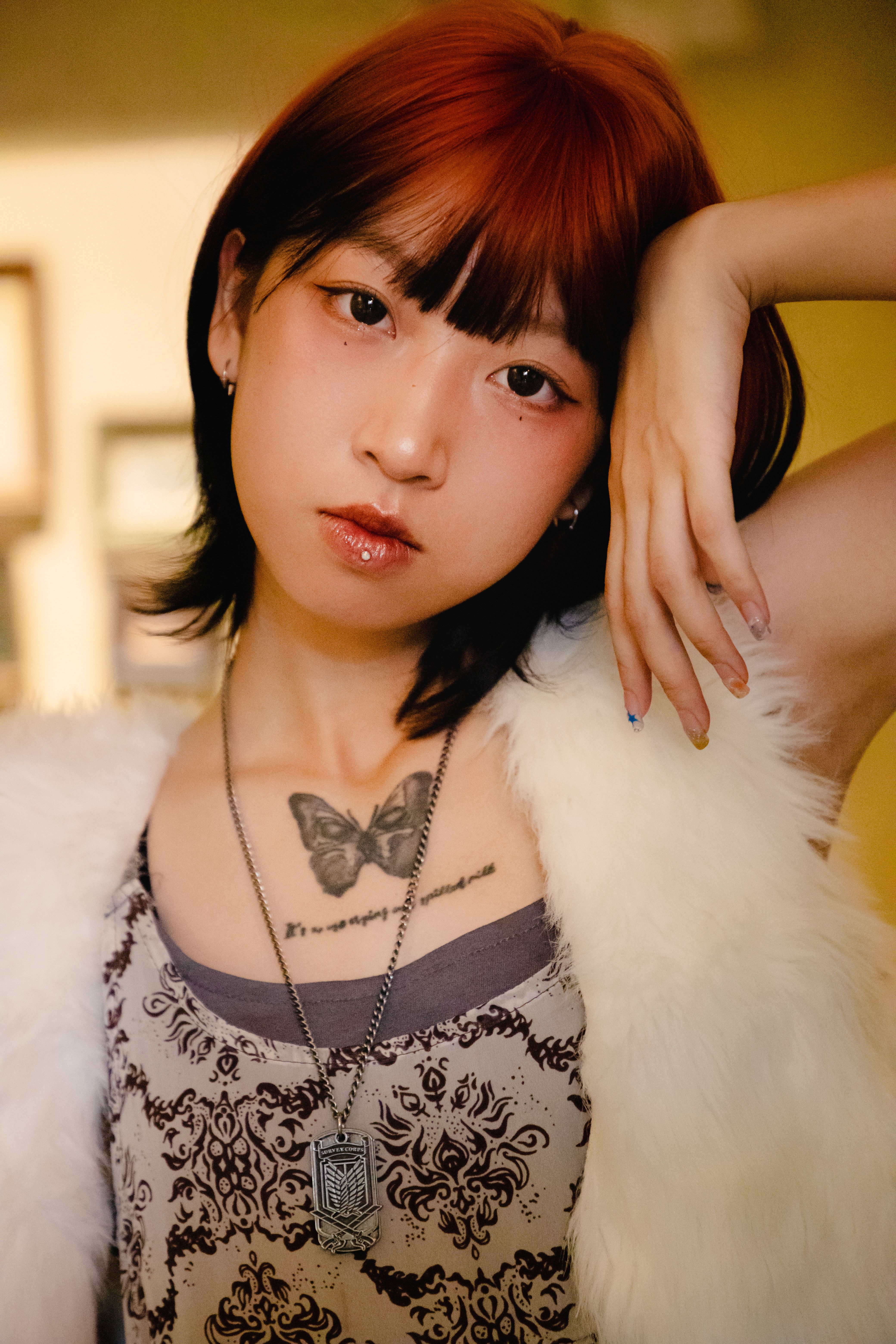 A young woman showcases her tattoo and stylish outfit in a confident pose indoors.