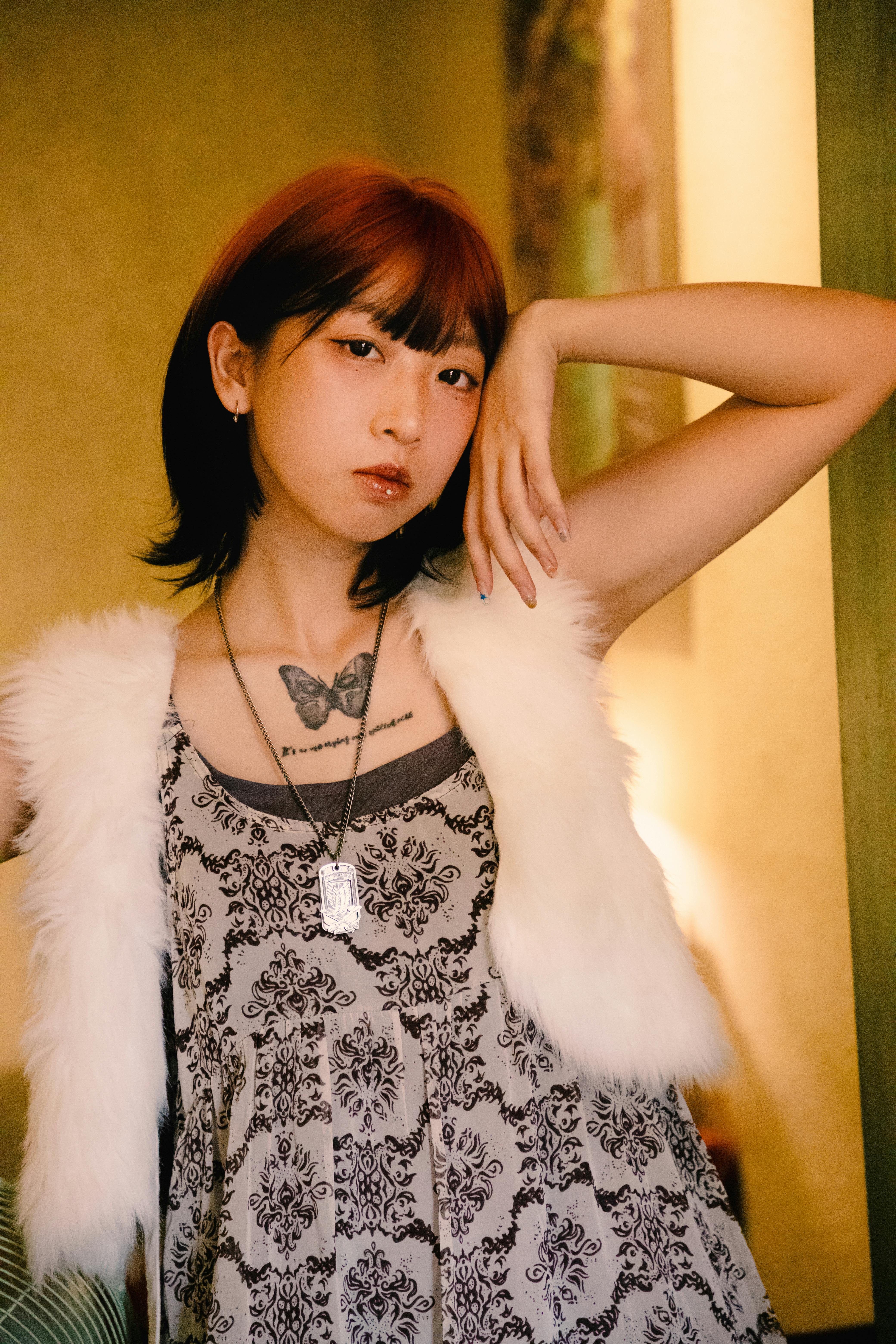 Young woman posing indoors, showcasing butterfly tattoo and trendy fashion.
