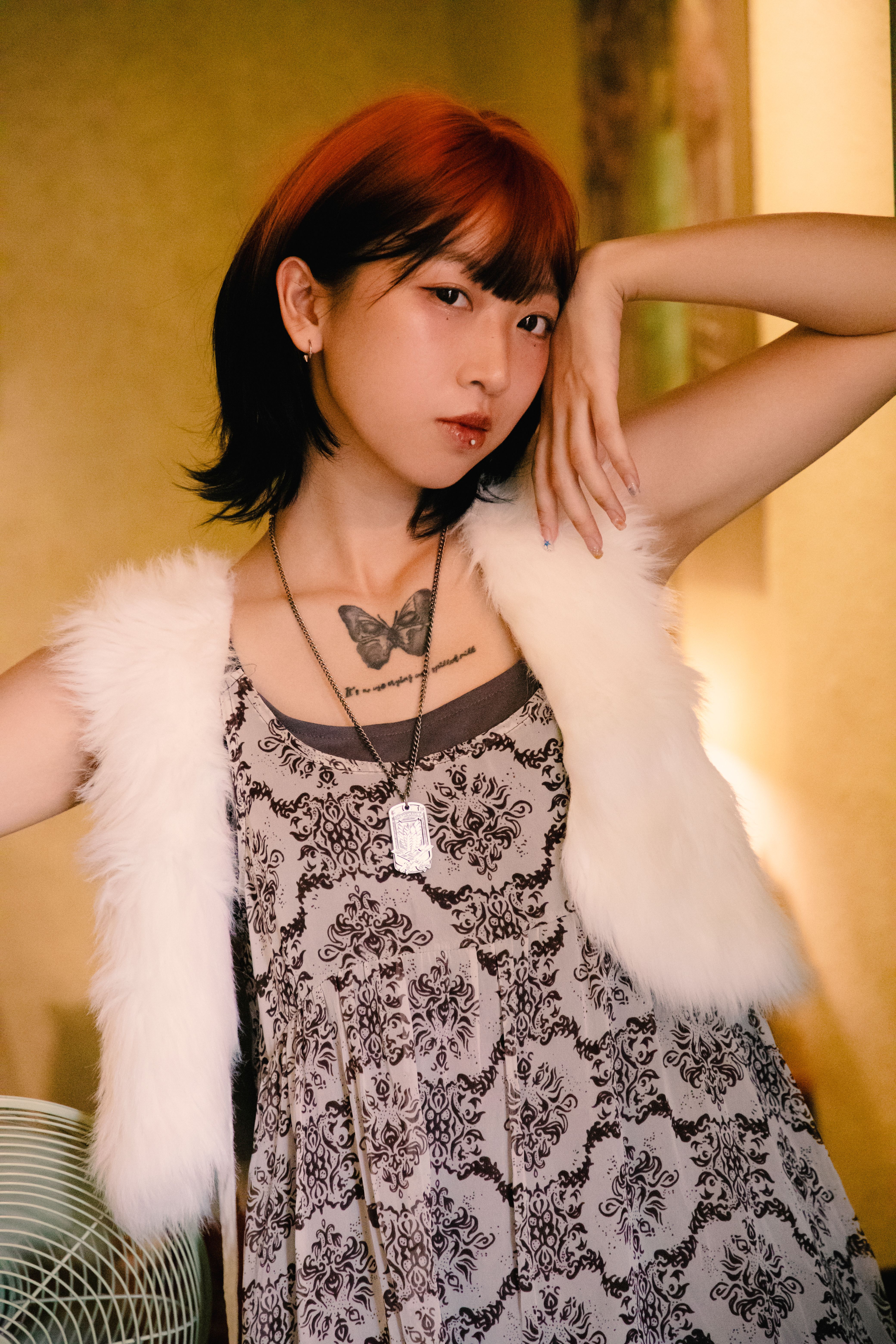 Trendy young woman with a butterfly tattoo in a stylish outfit, posing indoors.