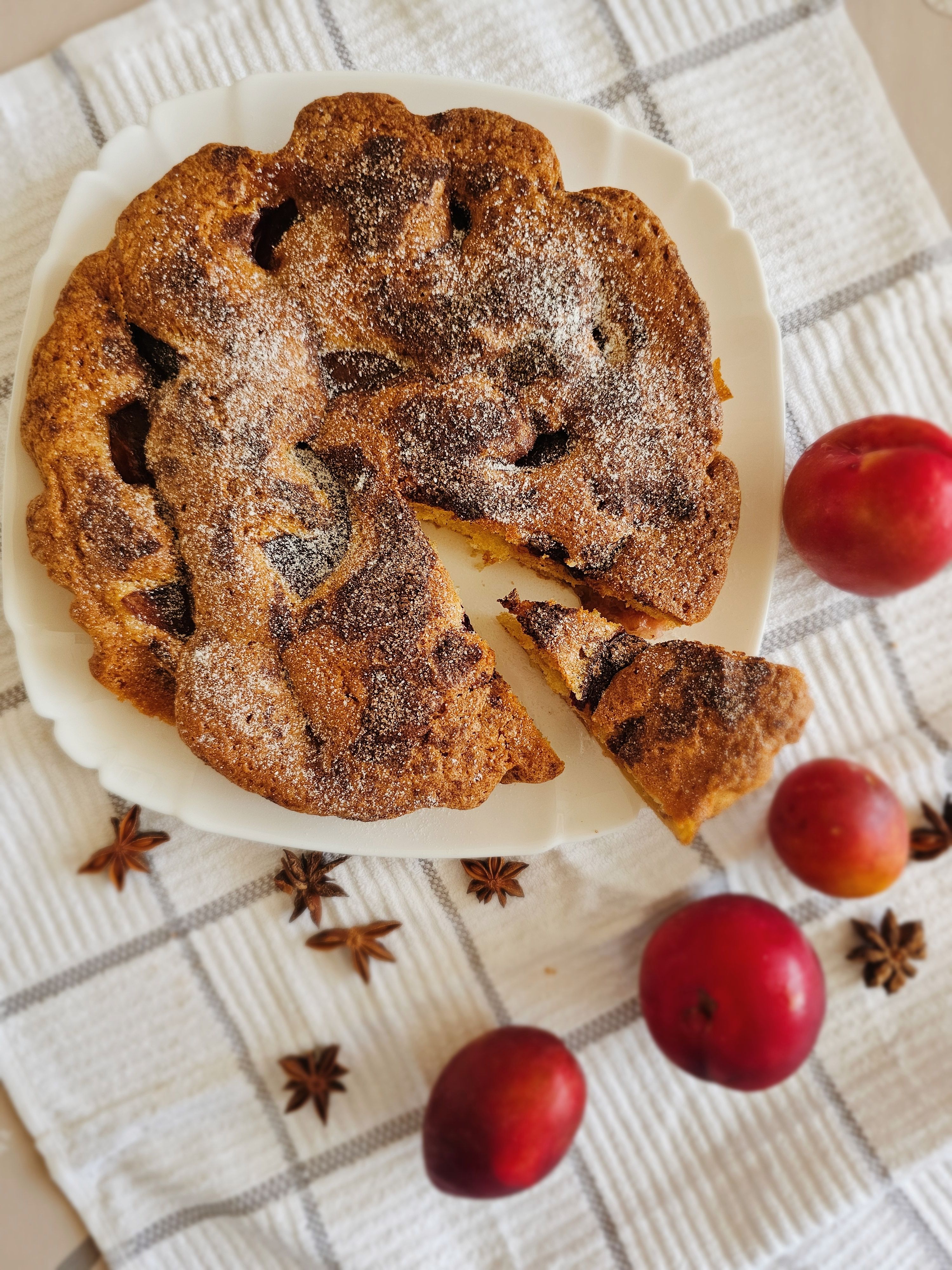 Flatlay of a baked plum cake with star anise and fresh plums.