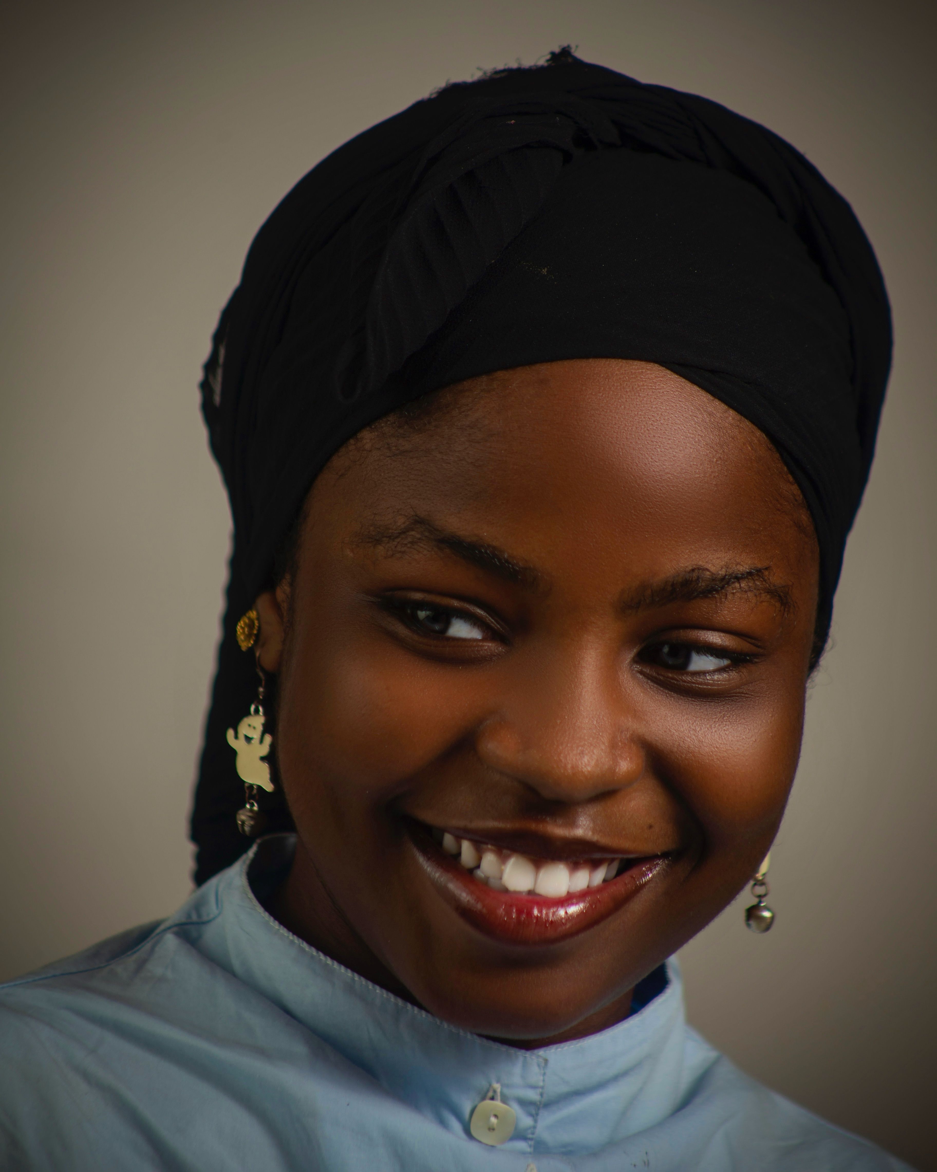 Close-up portrait of a smiling woman in a black headscarf, warm lighting.