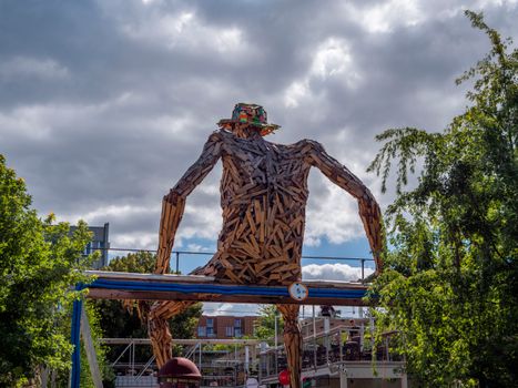 Large wooden sculpture in urban outdoor setting with clouds.