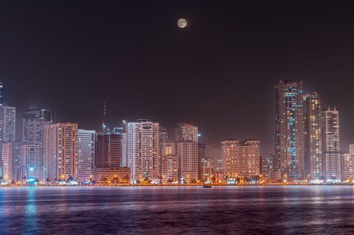 Free Scenic night view of Sharjah skyline with a full moon reflecting on the water. Stock Photo