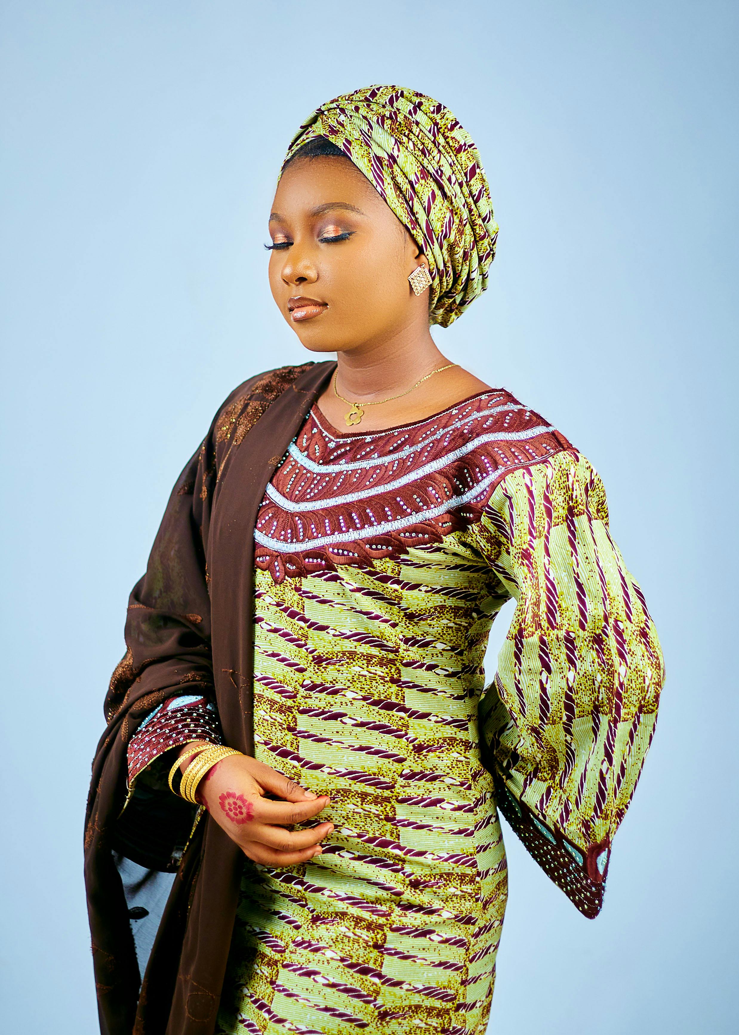 Portrait of a woman in vibrant traditional African attire against a light background.