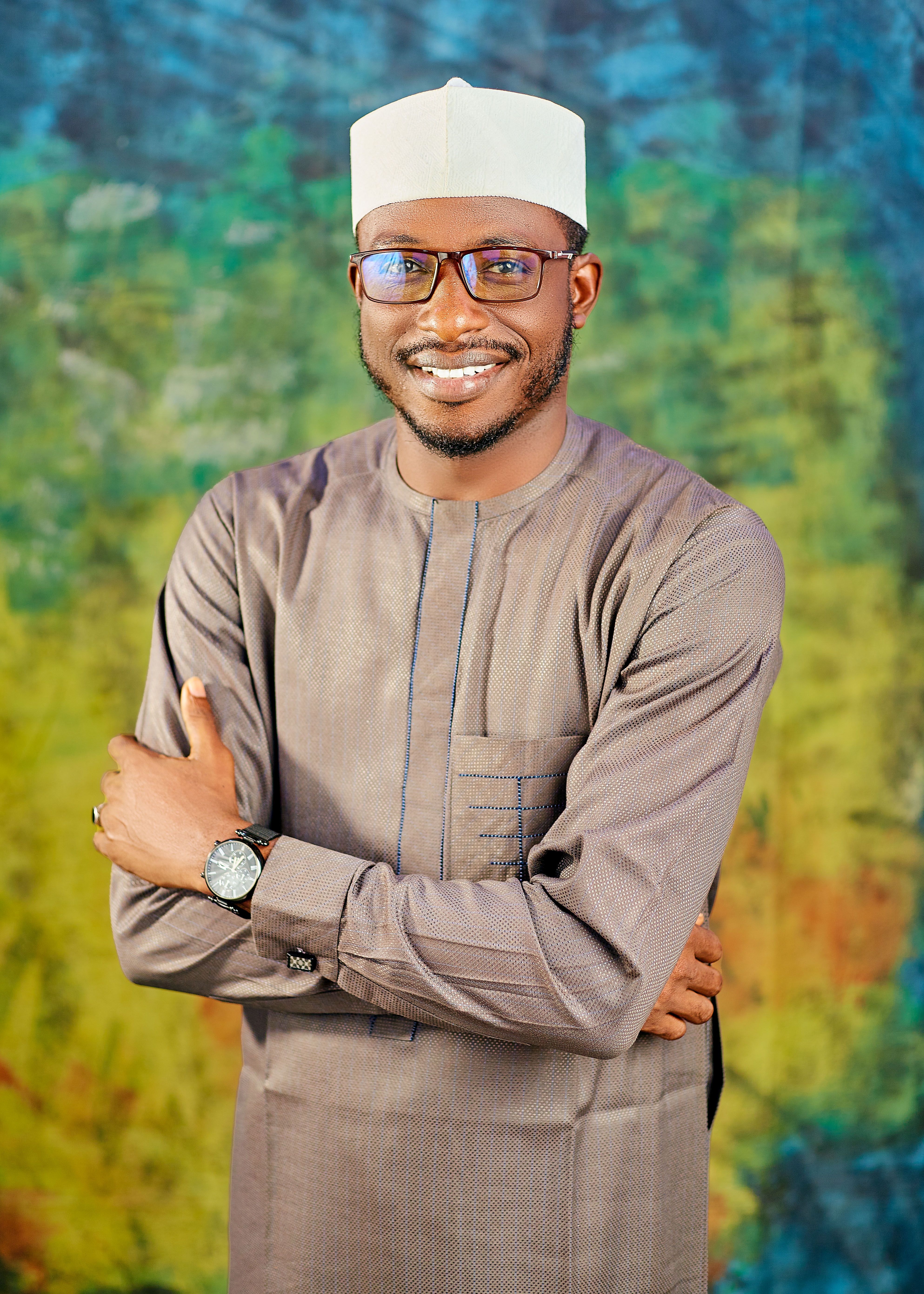 A cheerful man posing confidently in traditional attire with a colorful backdrop.