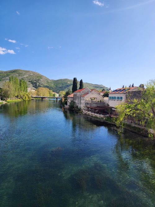 Free Peaceful riverside view of a traditional village with stone buildings and lush green hills. Stock Photo