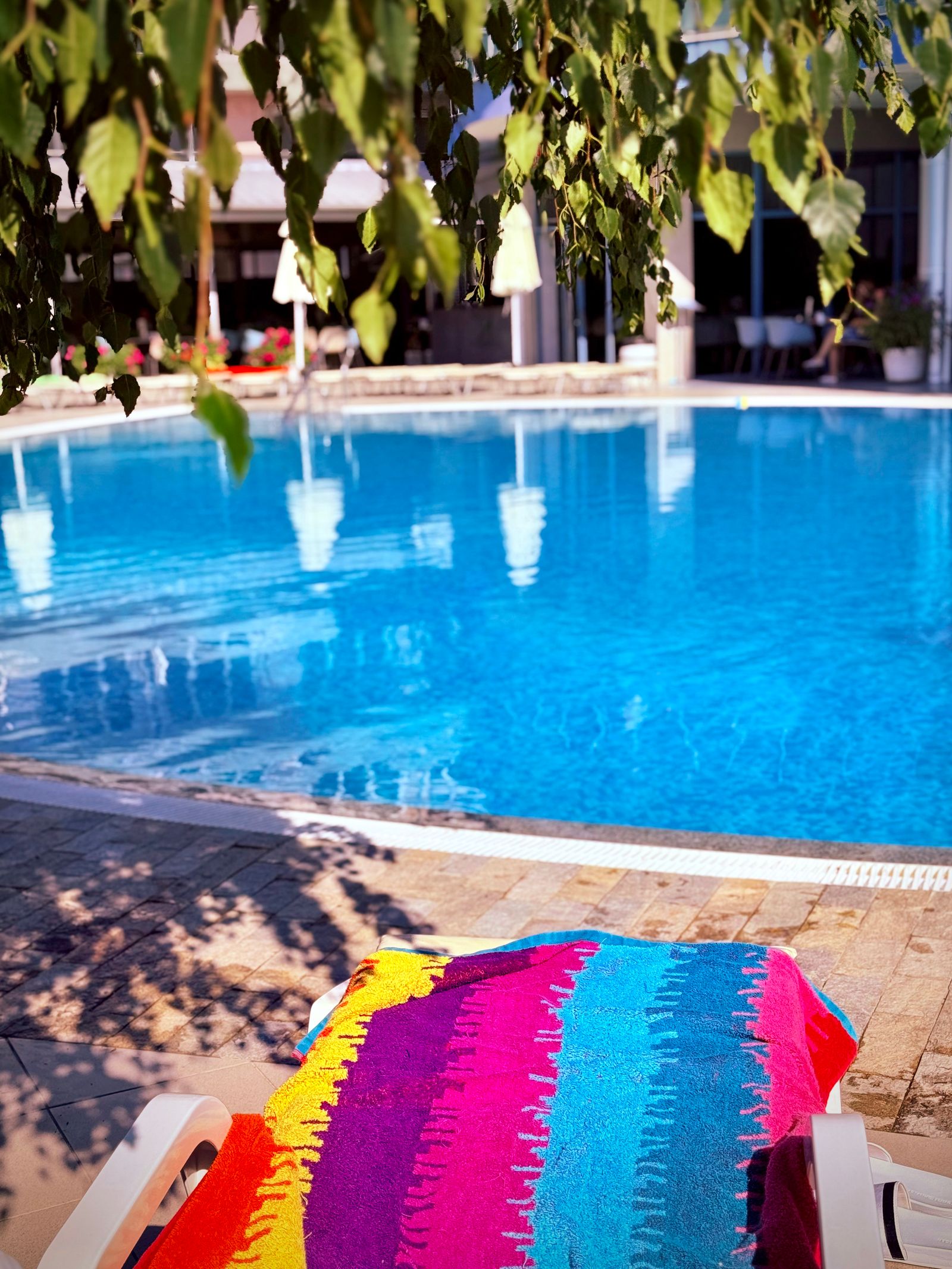 A rainbow-striped towel on a lounger beside an outdoor pool