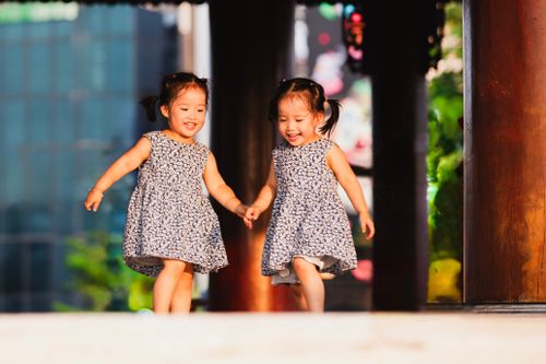Free Two joyful young girls in matching dresses run and play outdoors, capturing the essence of childhood happiness. Stock Photo