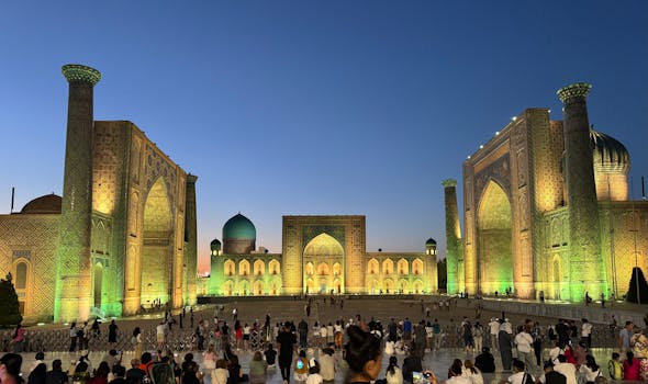 Evening view of Registan Square in Samarkand, with illuminated historic architecture and crowd.