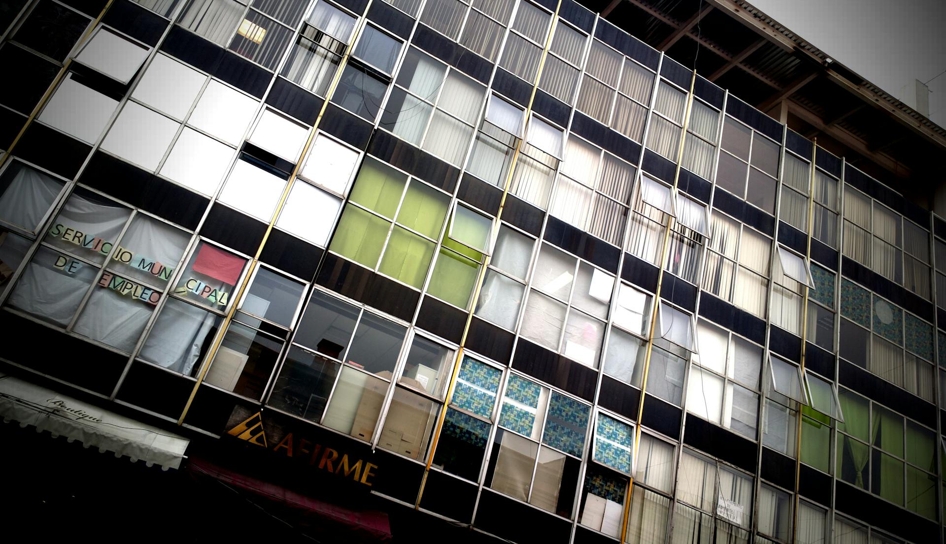 Modern urban office building facade featuring diverse window patterns and reflections.