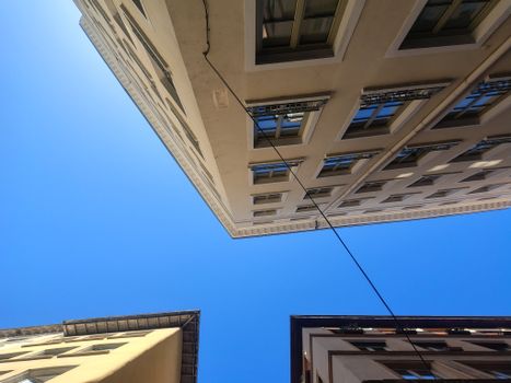 Looking up at intersecting building facades with a clear blue sky above.