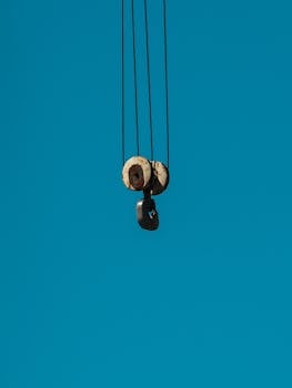 Aged metal pulley hanging against a clear blue sky, industrial minimalism.