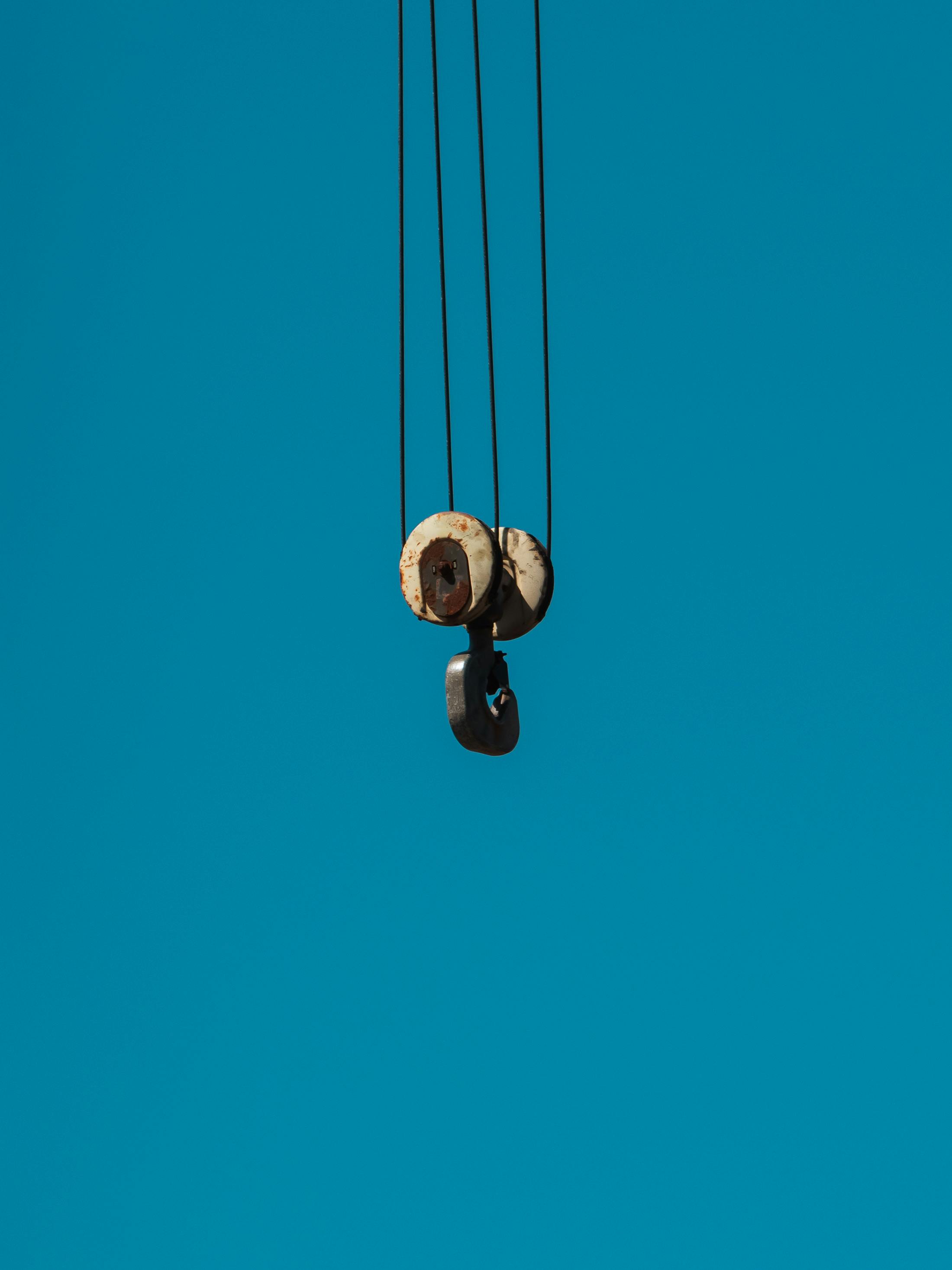 Free Aged metal pulley hanging against a clear blue sky, industrial minimalism. Stock Photo