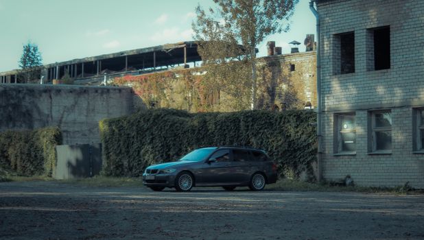 A BMW parked in an abandoned, cinematic environment with overgrown greenery and industrial backdrop.