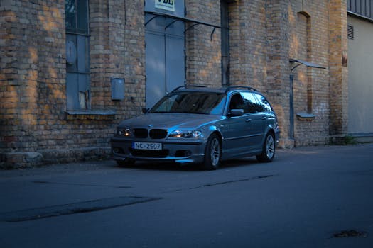 Vintage BMW car parked beside an old brick building in a moody urban setting.