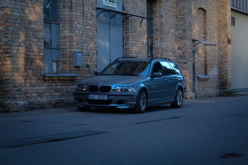 Free Vintage BMW car parked beside an old brick building in a moody urban setting. Stock Photo