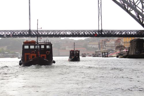 Free Wooden boats on the Douro River under the iconic Dom Luís I Bridge in Porto, Portugal. Stock Photo