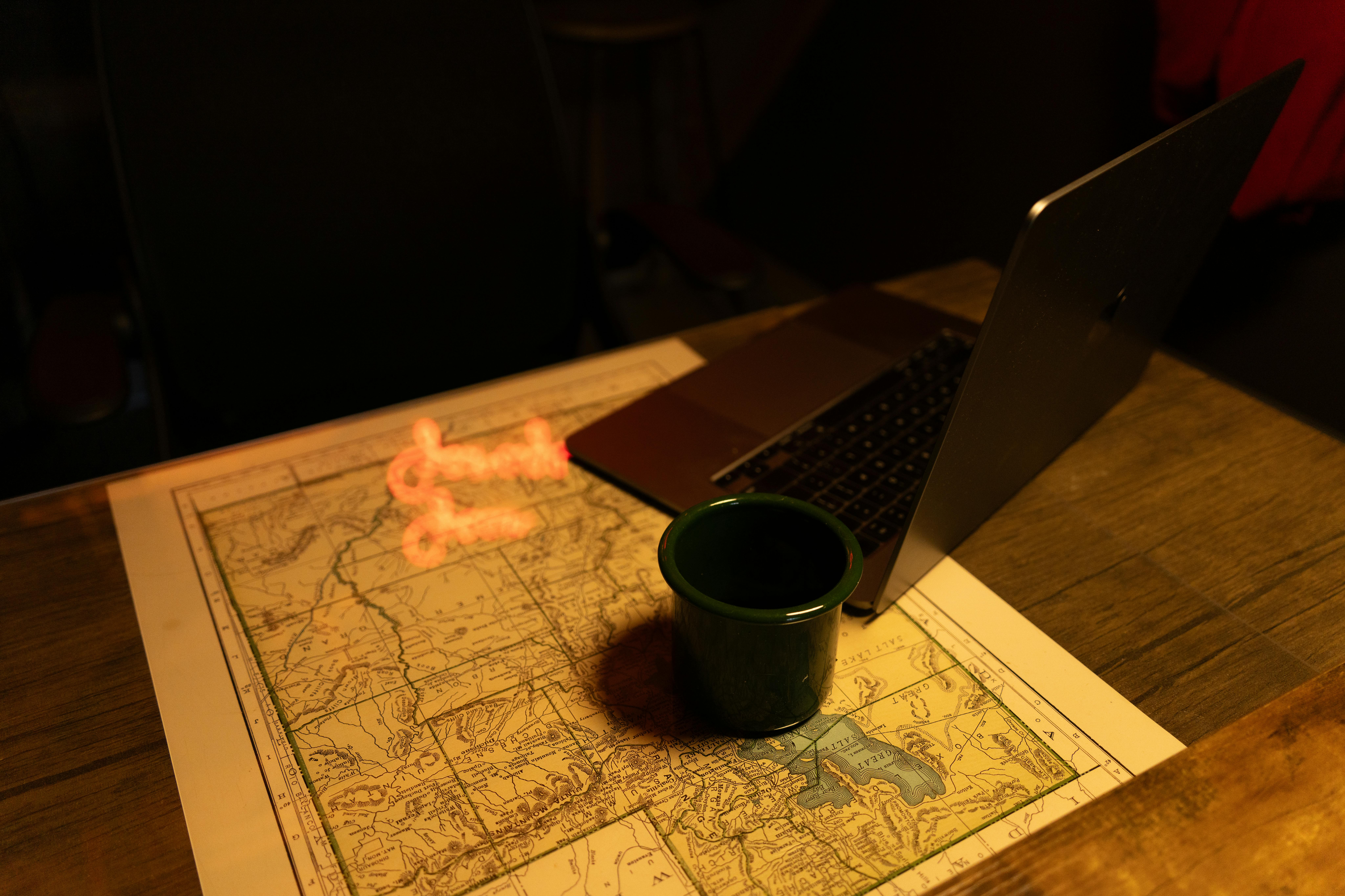 Kostnadsfria En mysig, svagt upplyst arbetsplats med karta, laptop och kaffekopp, som väcker kreativitet och utforskande. Stock foto