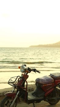 Vintage red motorcycle parked by a tranquil beach at sunset, highlighting a peaceful coastal view.