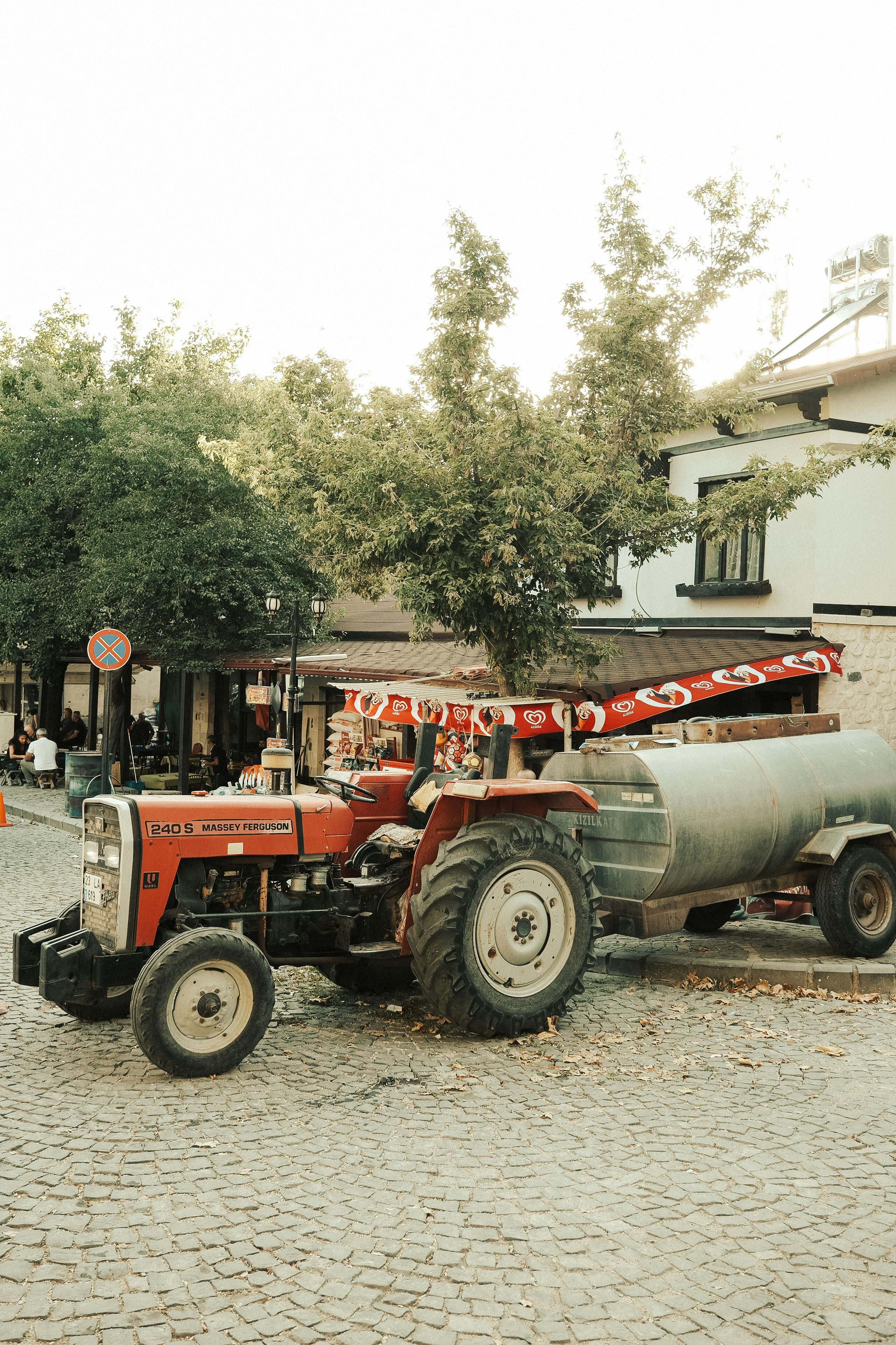 A red tractor parked on a cobblestone street in a charming town square.