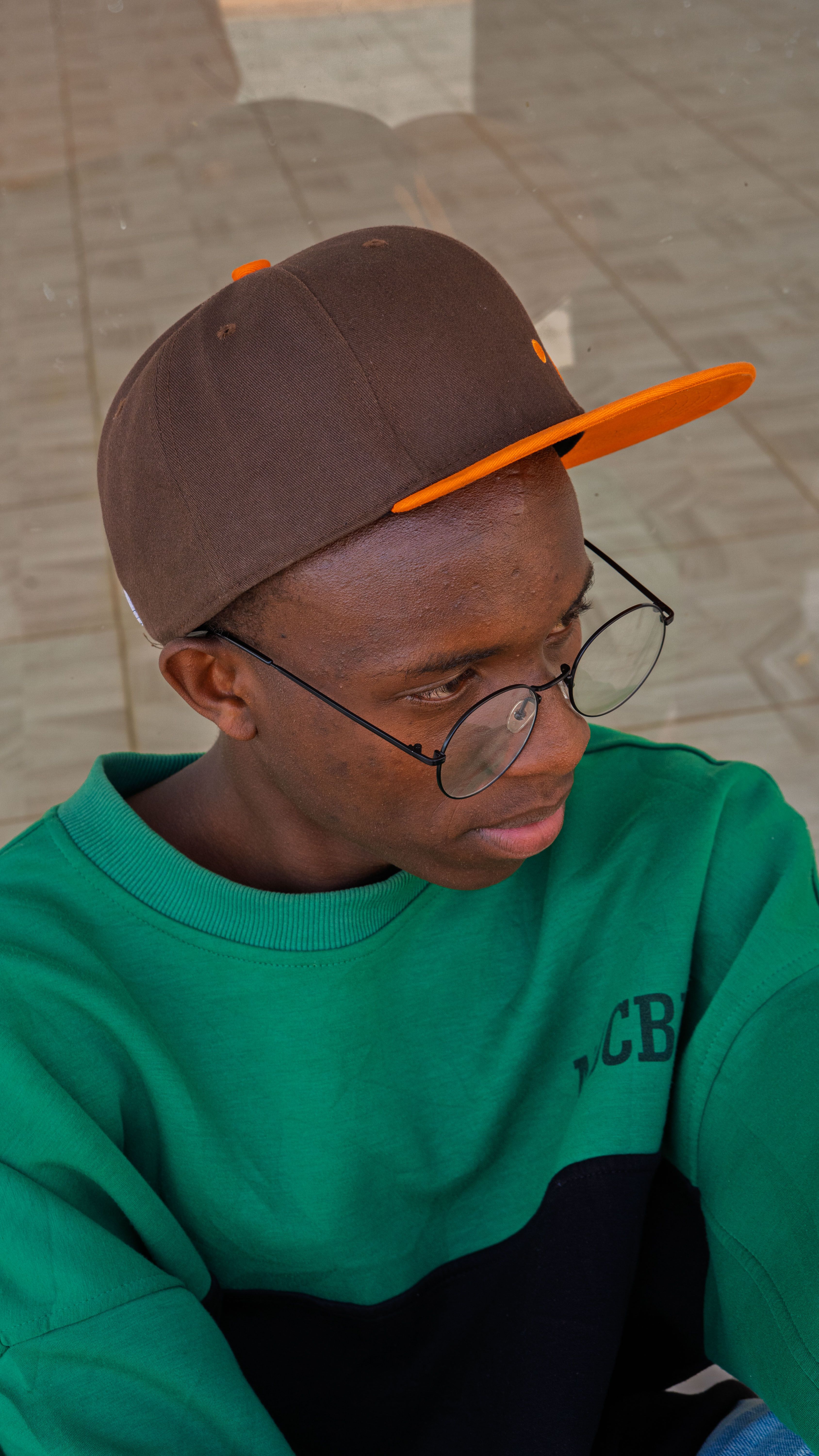A portrait of a young man wearing glasses and a cap, showcasing casual urban fashion style.