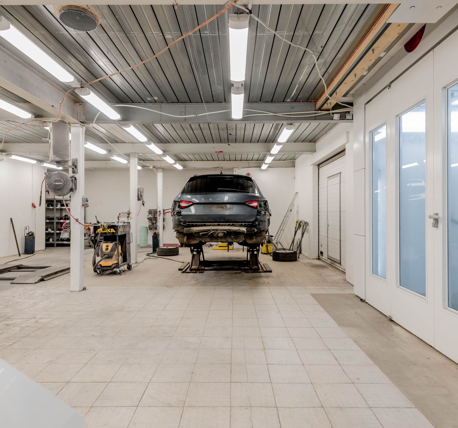 Well-lit garage with a car on a hydraulic lift ready for repair.
